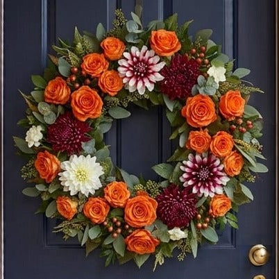 Fall door wreath with orange roses, white and burgundy dahlias and chrysanthemums, close-up on a navy front door
